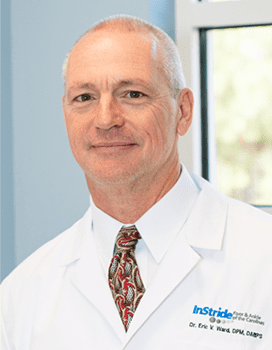 Man in white lab coat smiles at the camera, tie visible, light setting.