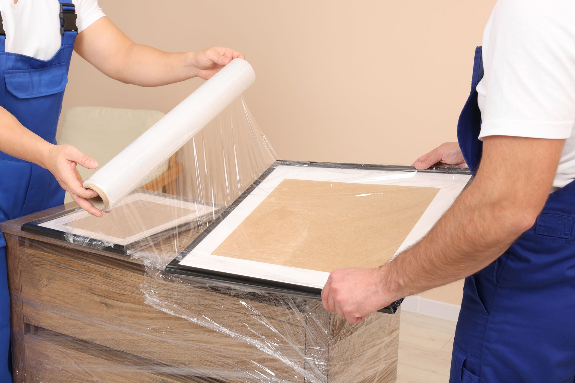 Movers wrapping framed artwork with plastic wrap.