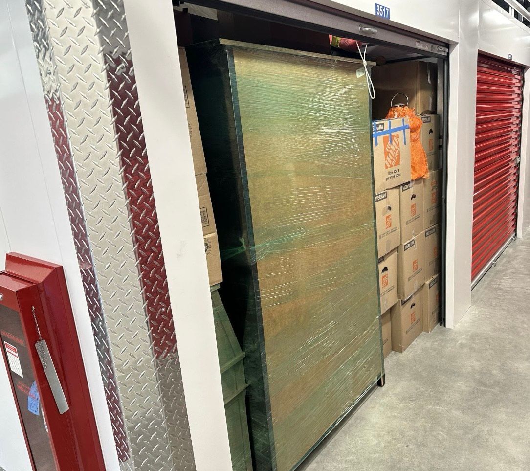 Storage unit with a partially open door revealing boxes. The unit is in a hallway with other units.
