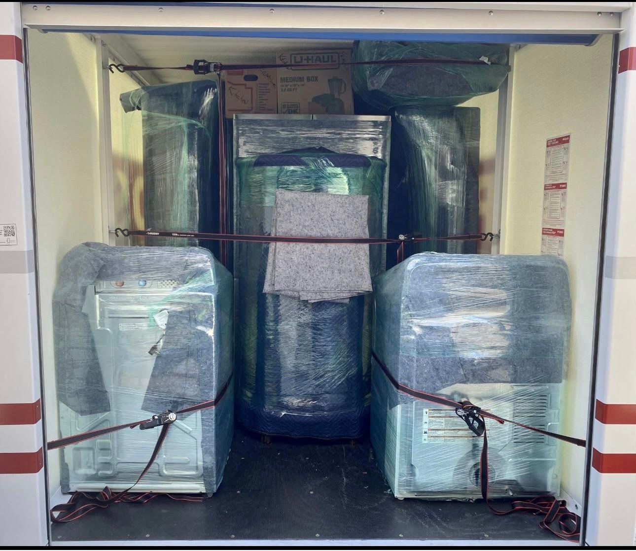 Moving truck cargo area packed with wrapped appliances, secured with straps.