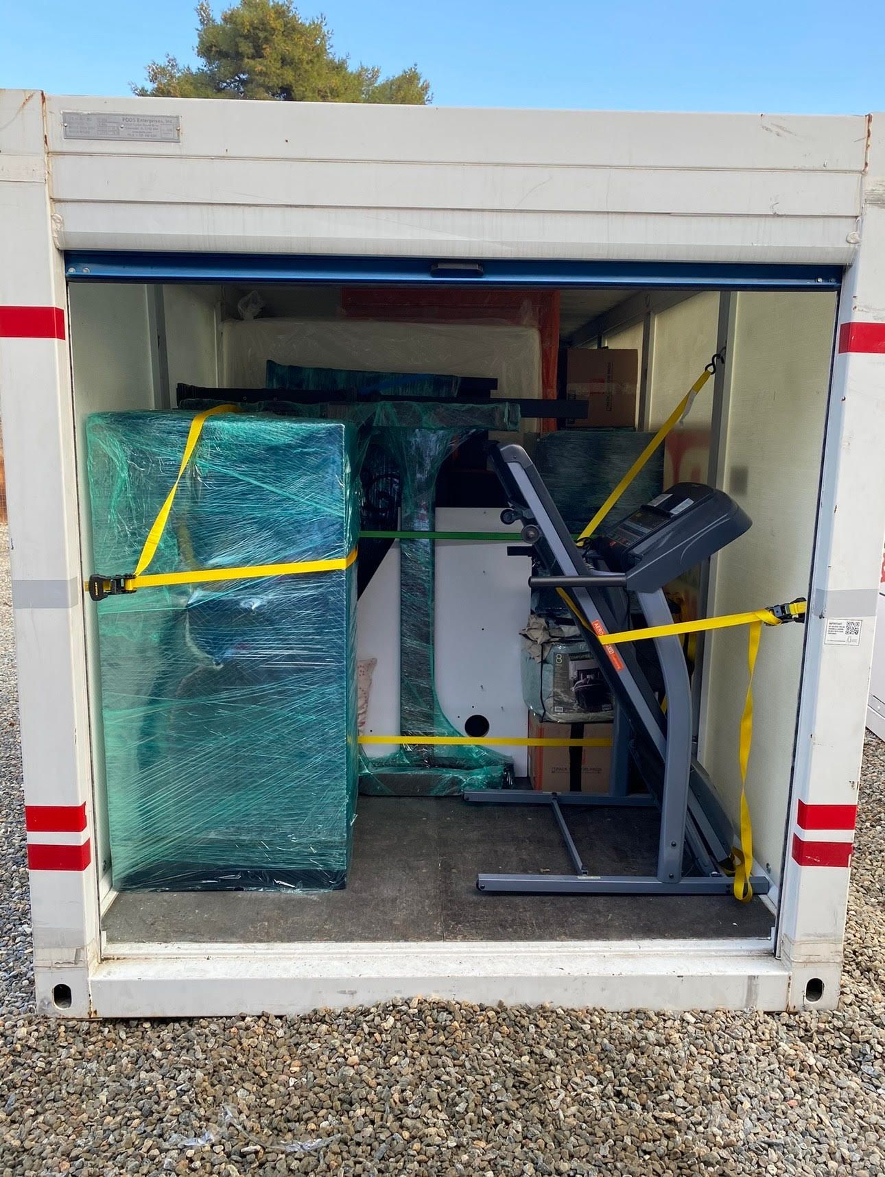 A white storage container with items inside. Wrapped furniture and a treadmill secured with yellow straps.