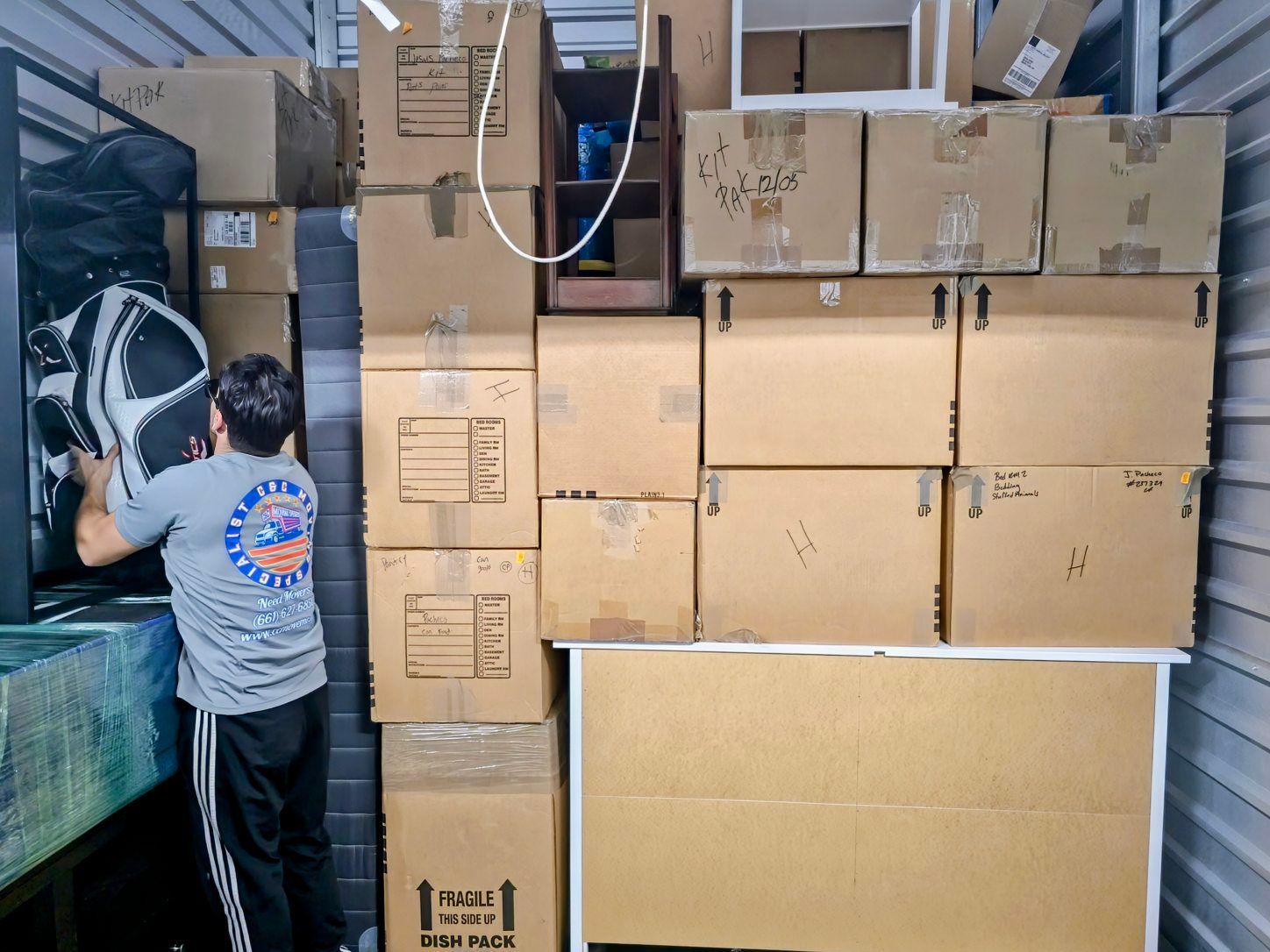 A man is carrying a stack of boxes in a storage room.