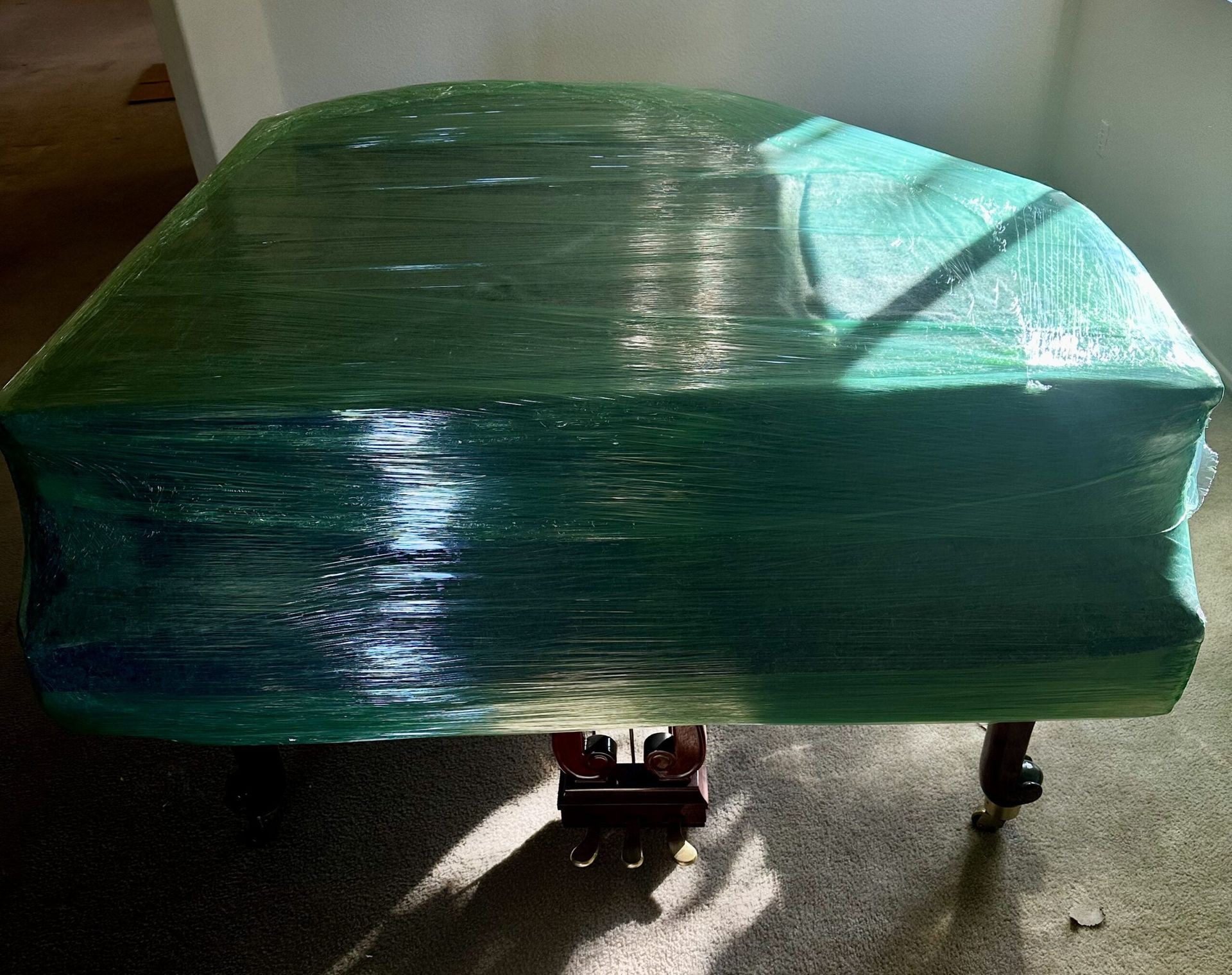A green piano is wrapped in plastic and sitting on the floor