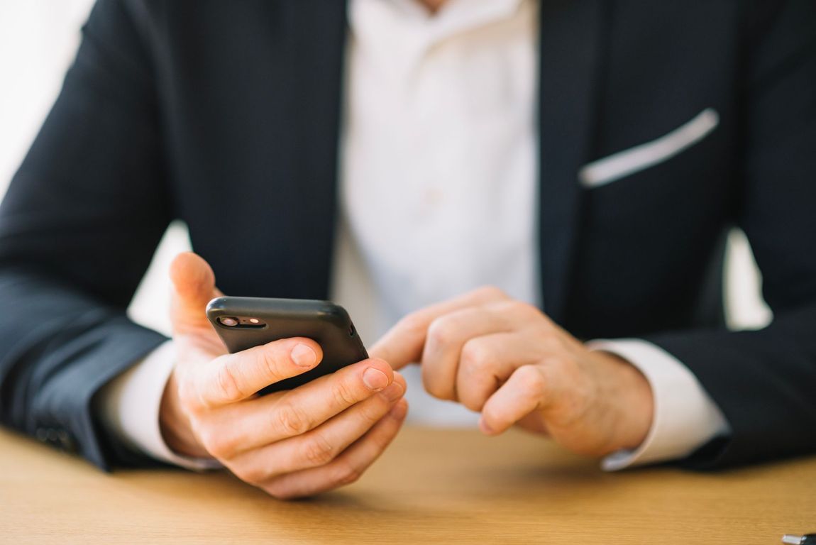 A man in a suit is sitting at a table using a cell phone.