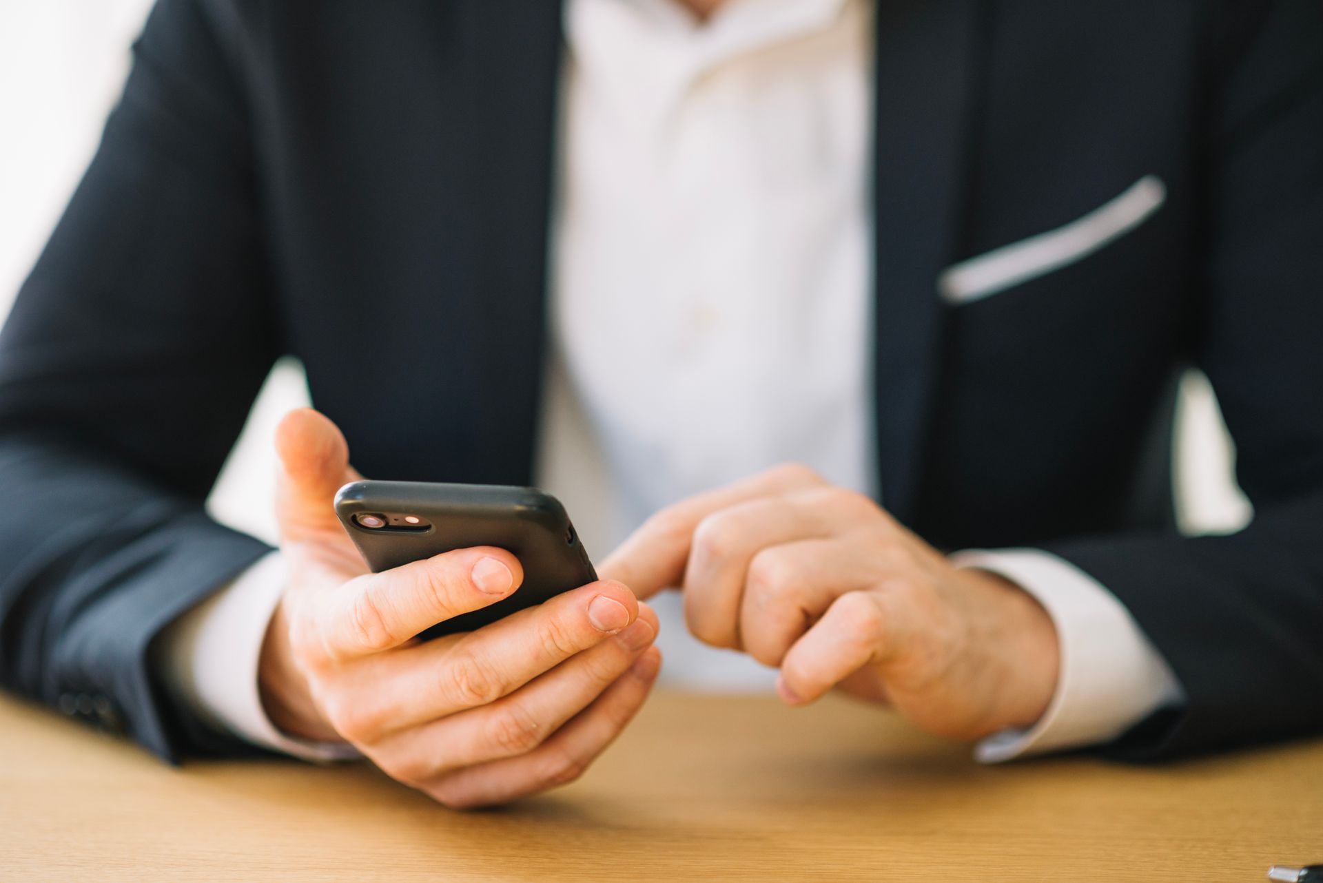 A man in a suit is sitting at a table using a cell phone.