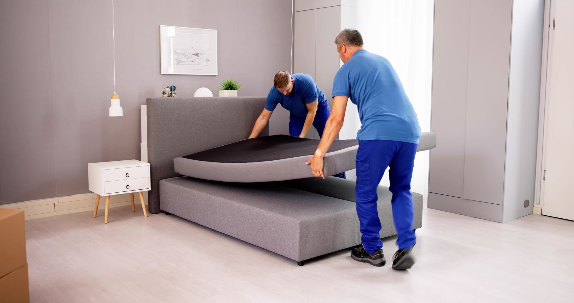 Two men are working on a bed in a bedroom.