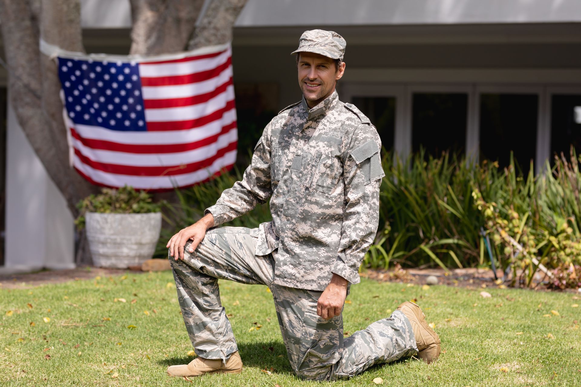 A man in a military uniform is kneeling in front of an american flag.
