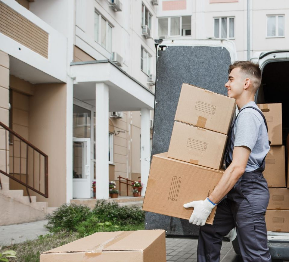 Man carrying boxes from a moving truck into a building.