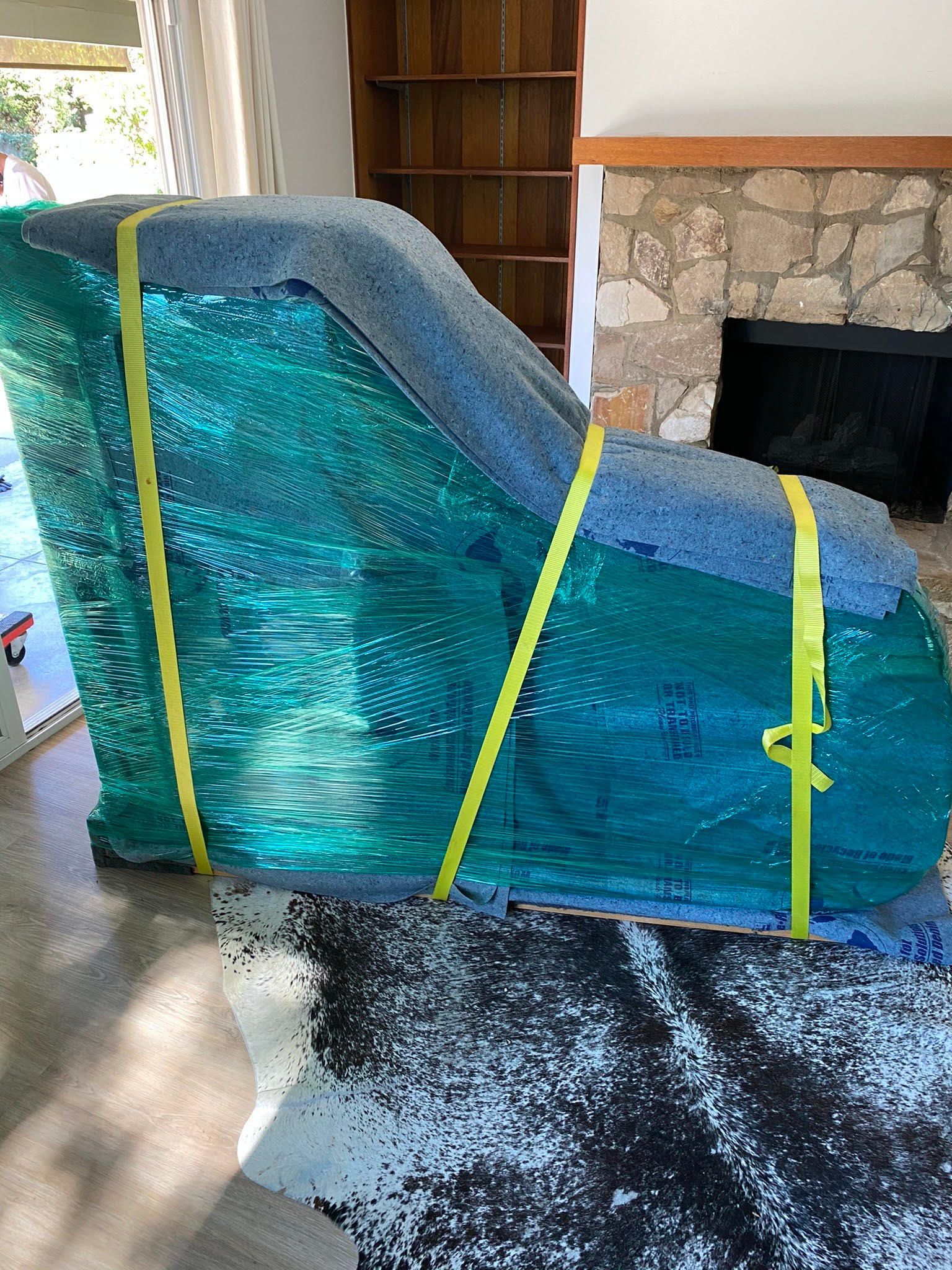 A green piano is wrapped in plastic and sitting on the floor