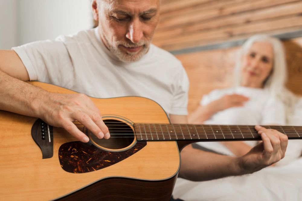 An elderly man is sitting on a couch with a cane and a nurse is standing next to him.