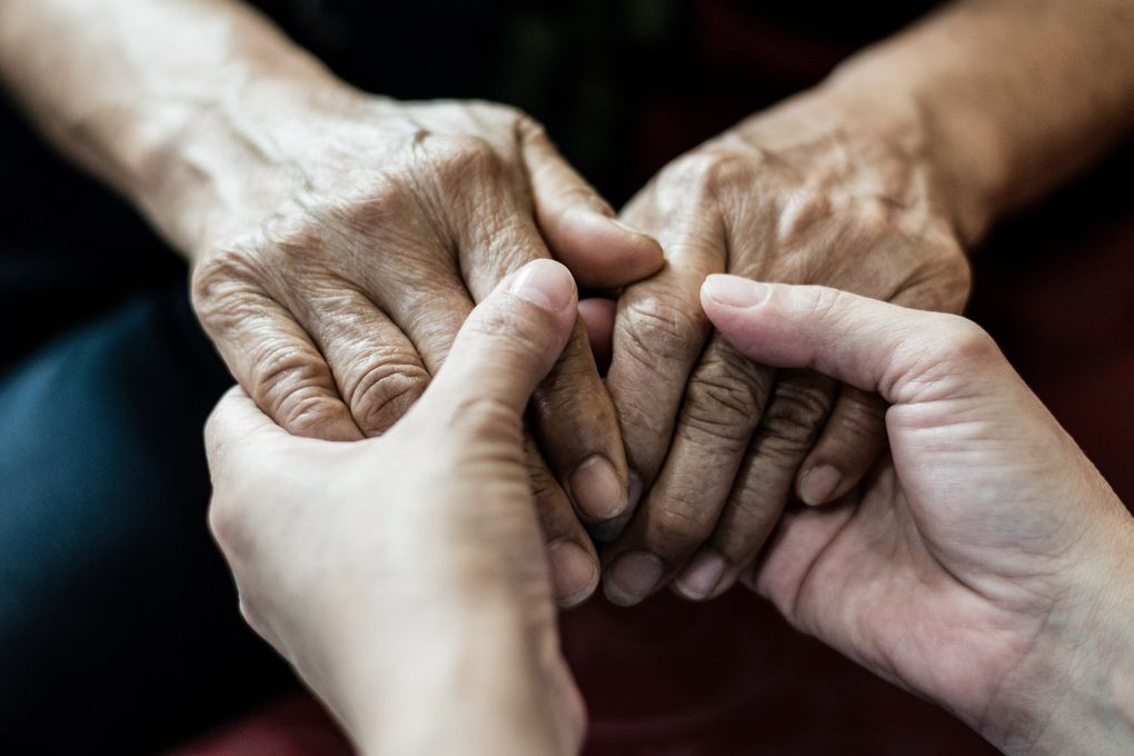 A young woman is holding the hands of an older woman.