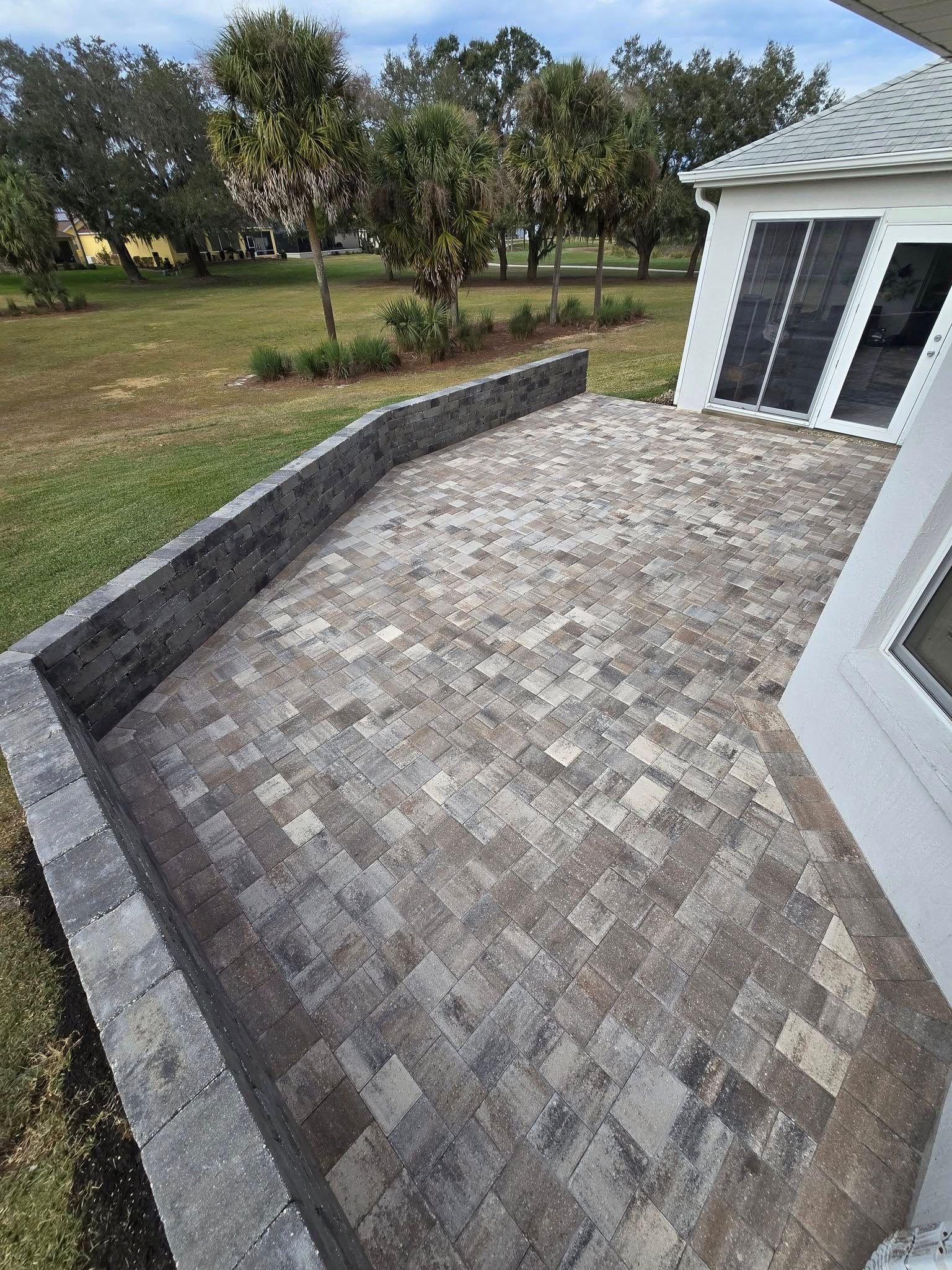 A brick walkway leading to a house with trees in the background.