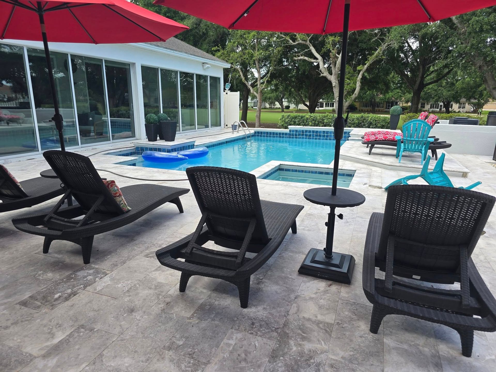 A patio with chairs and umbrellas in front of a swimming pool.