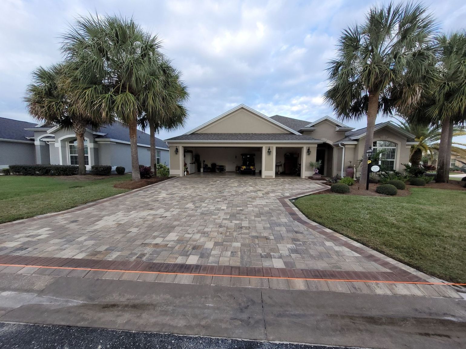 A large house with a brick driveway and palm trees in front of it