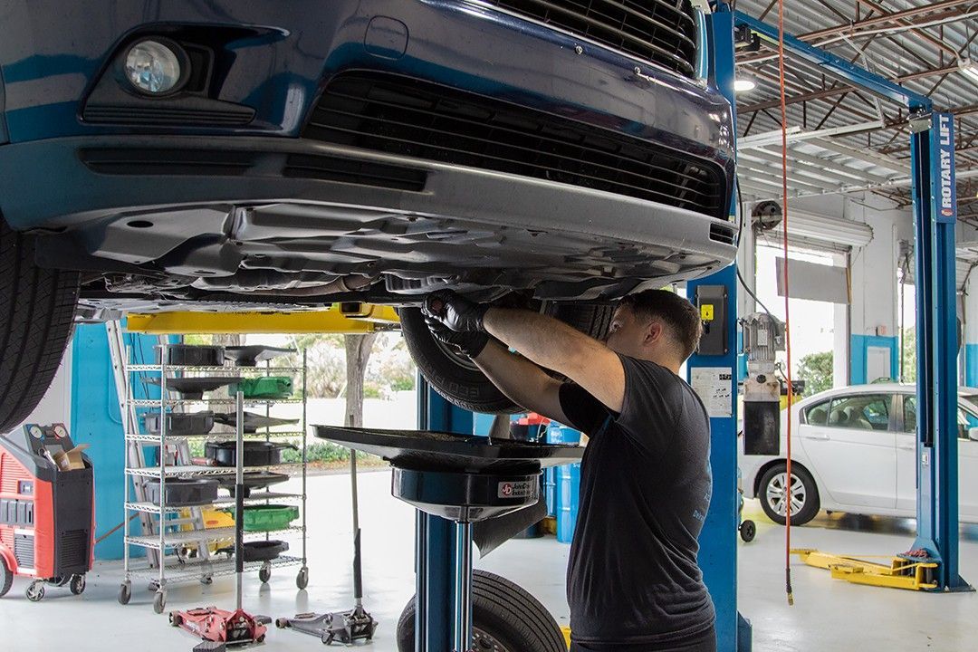 Mechanic working under a car in an auto repair shop, using a lift in a bright garage.