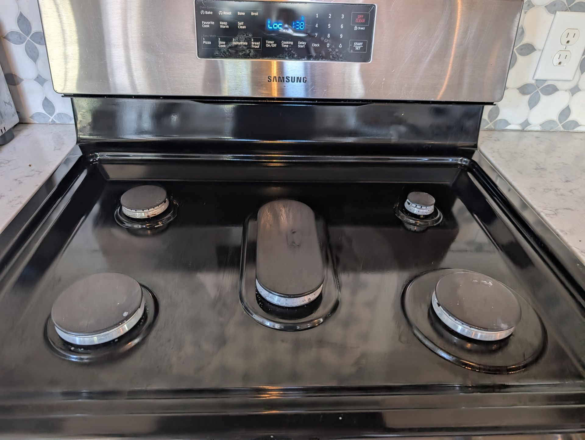 Black gas stovetop with four burners, control panel at the top, and silver trim.