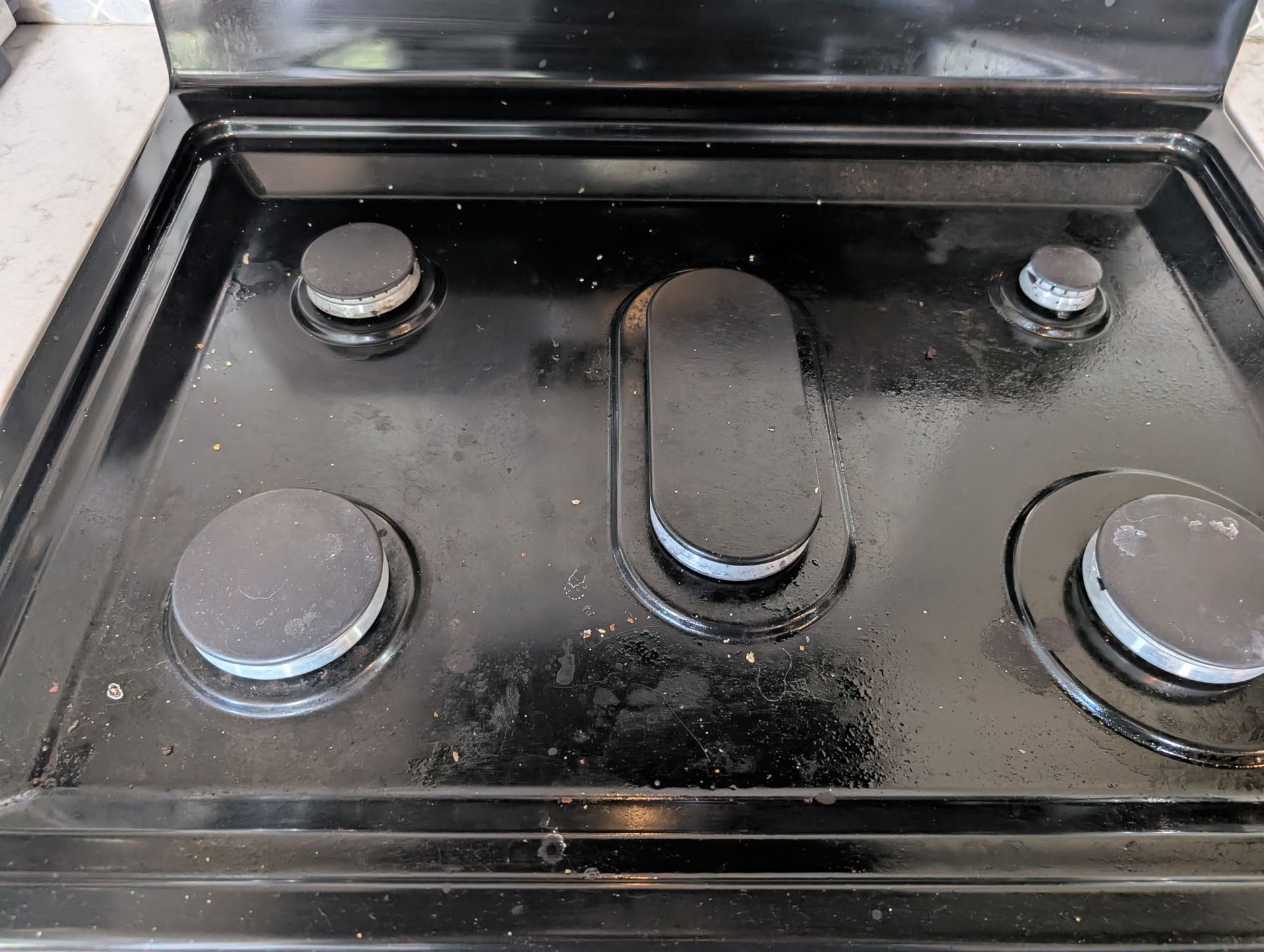 Black stovetop with four circular burners and one oval burner; surface has food residue.
