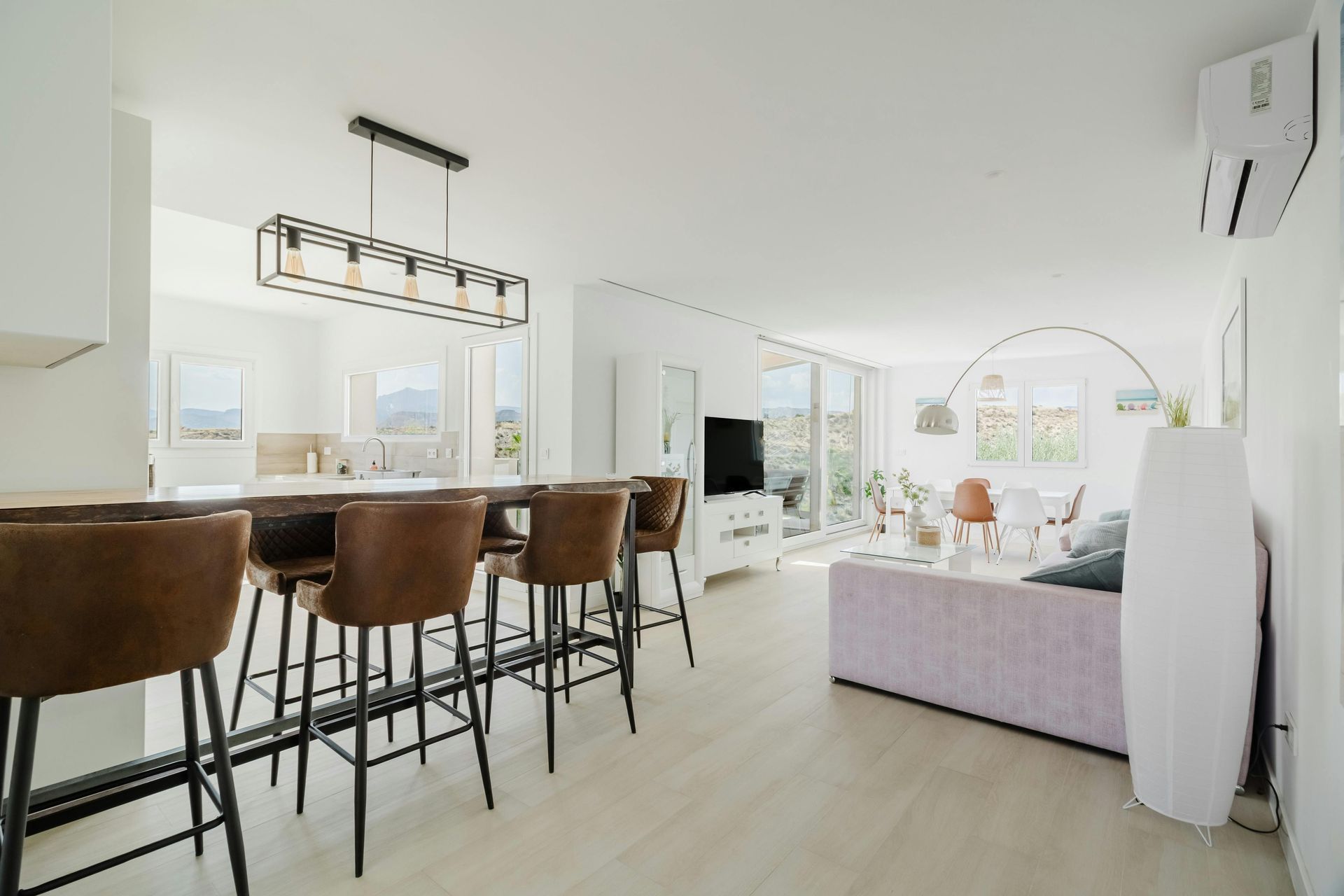 Modern open-plan living space with kitchen island, bar stools, and a living area with light purple sofa.