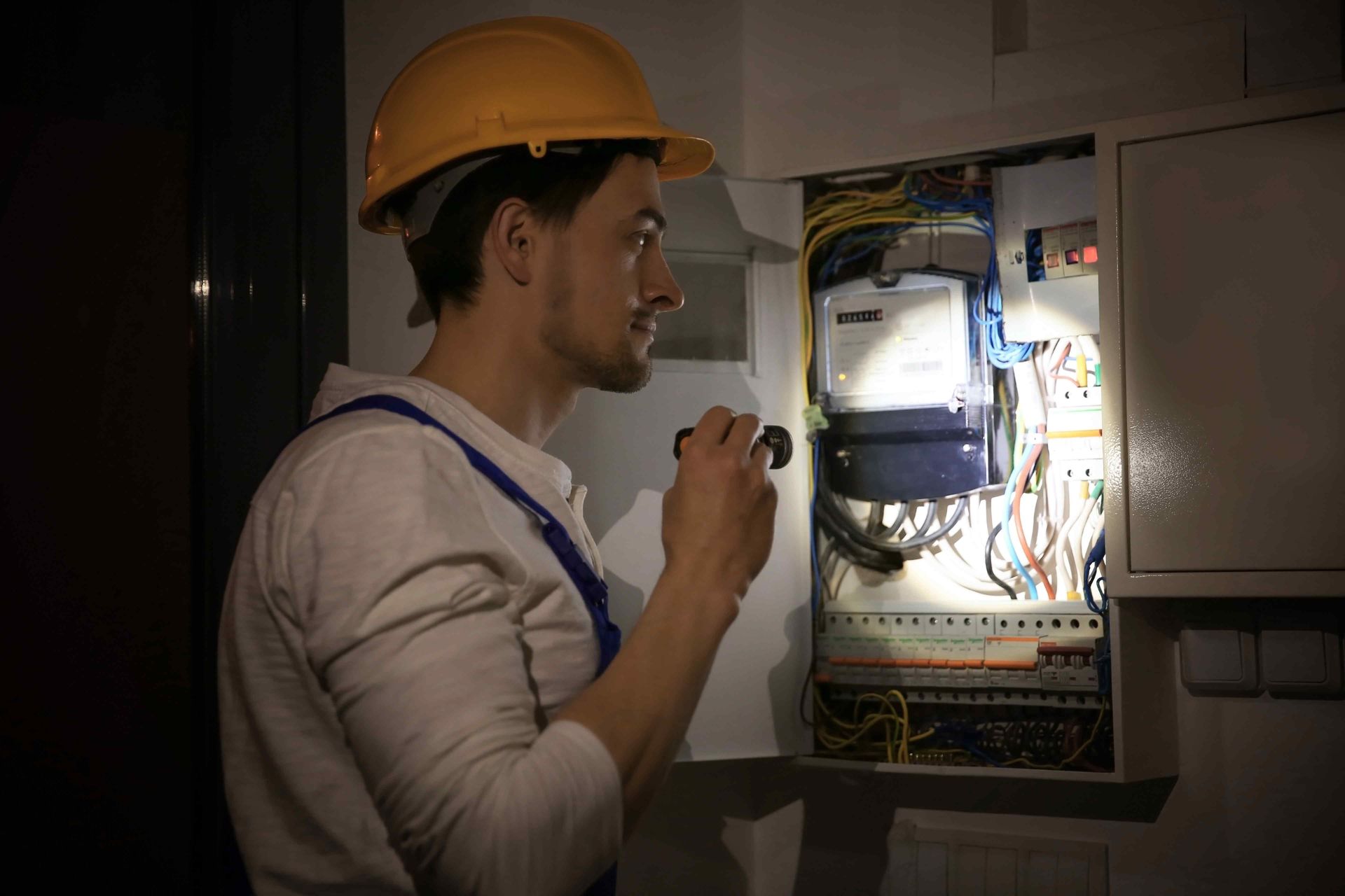 electrician using a flashlight to inspect a circuit breaker in the dark