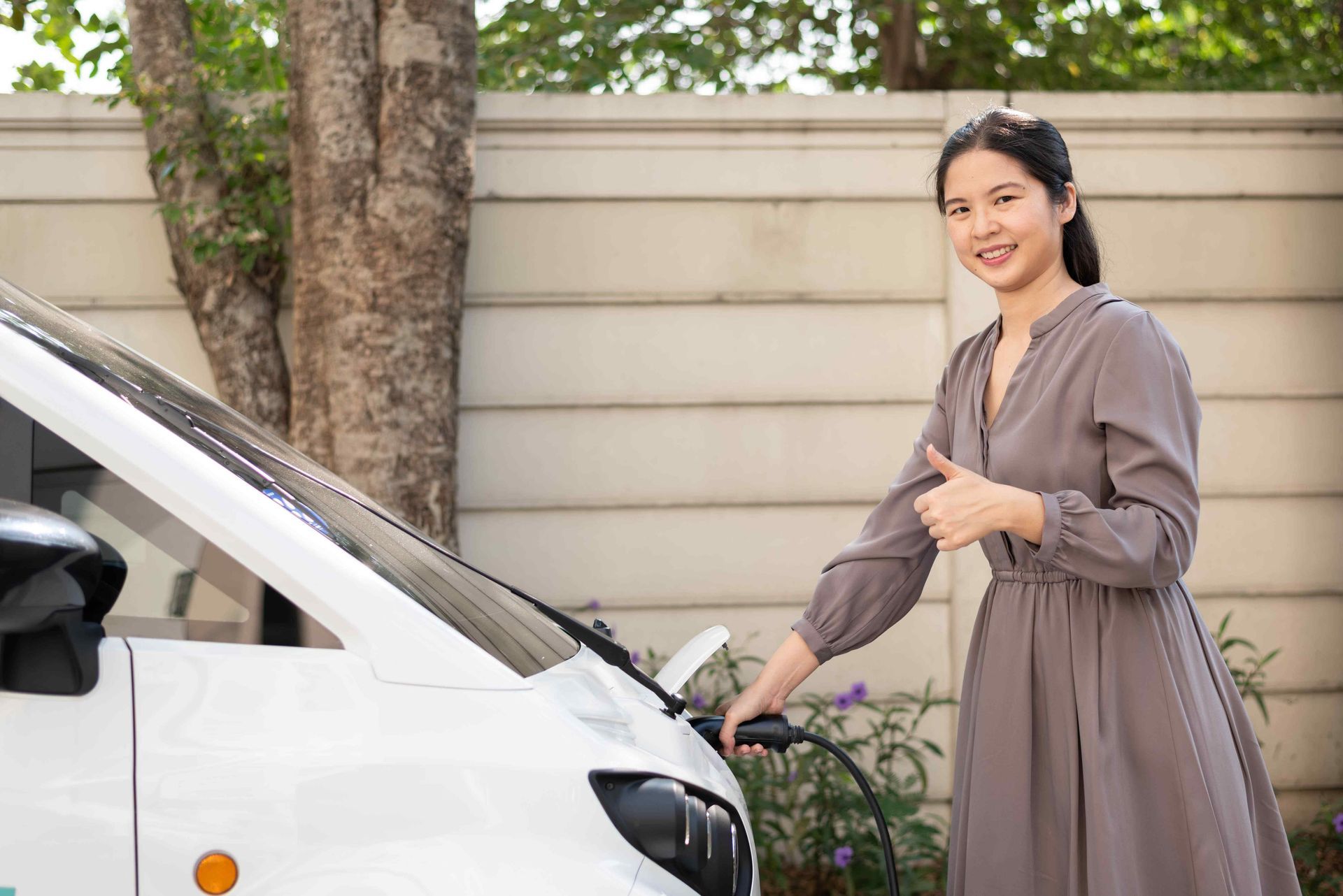 a woman charging her electric vehicle at home and giving a thumbs up
