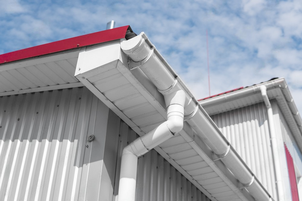 A white gutter on the side of a building with a red roof.