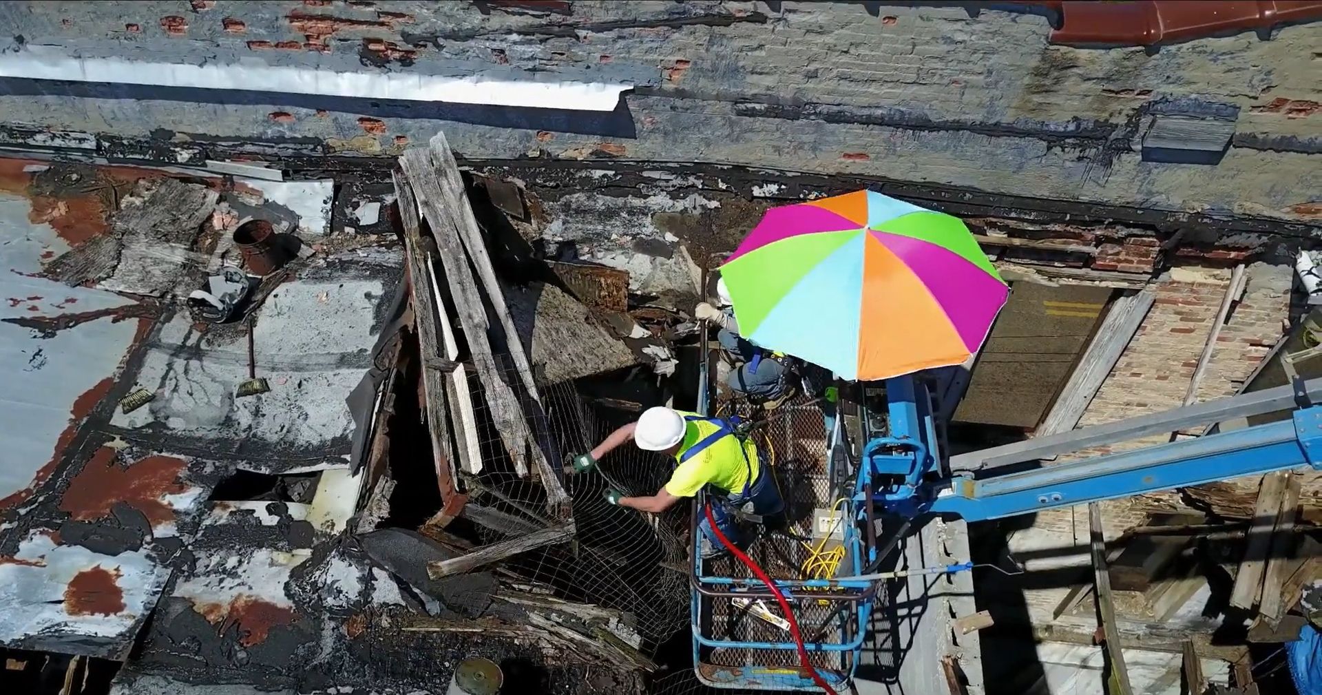 An aerial view of a construction worker in a bucket with an umbrella.