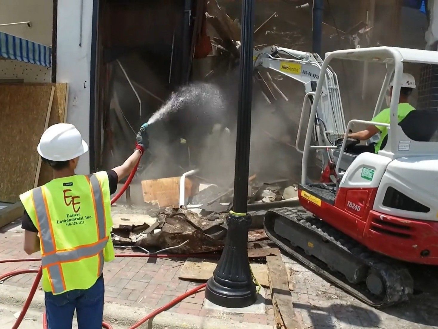 A construction worker is spraying water on a building with a hose.