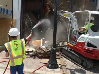A construction worker is spraying water on a building with a hose.