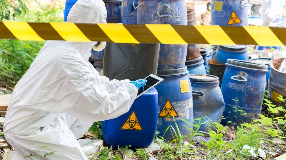 Person in protective clothing doing inventory on hazardous waste.