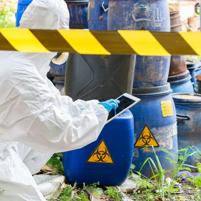 Hazmat worker in protective suit inspecting blue chemical waste barrels behind caution tape in Greenville SC.