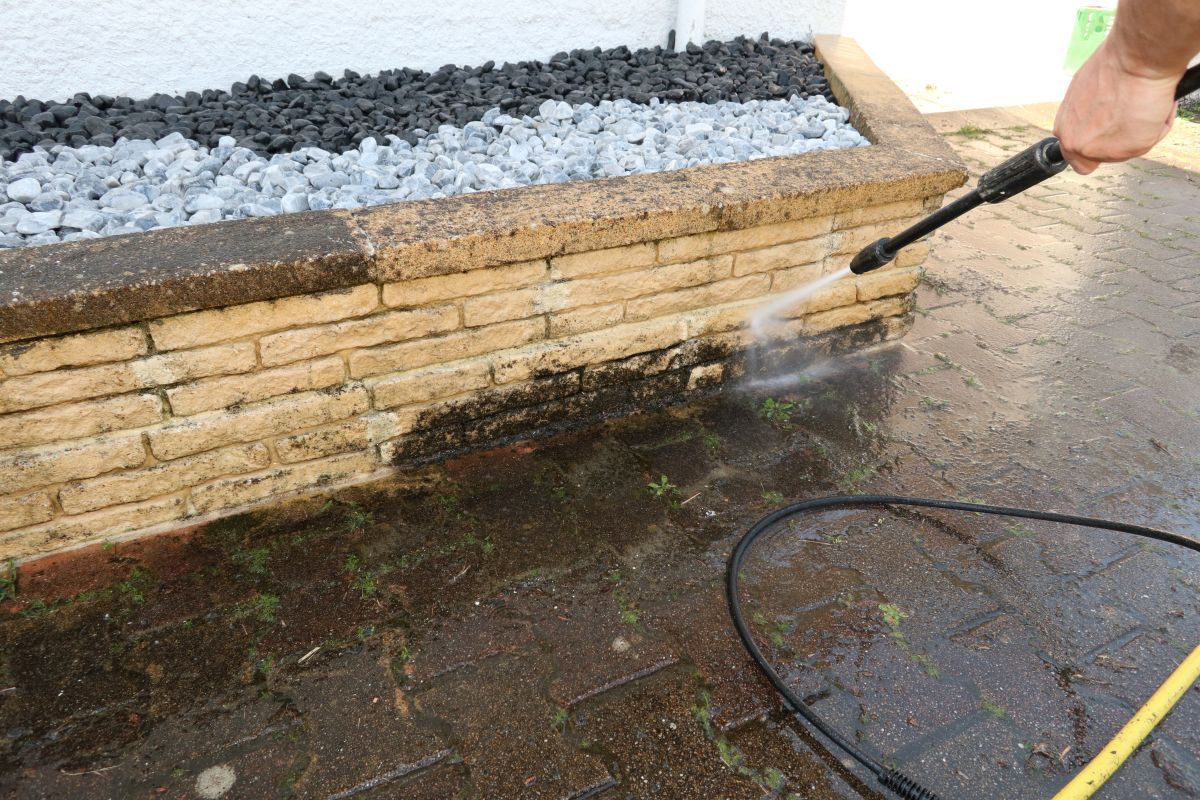 A person is using a high pressure washer to clean a brick wall.