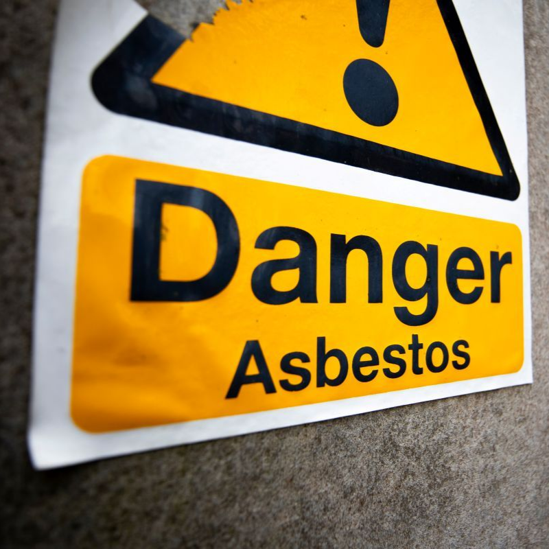 Yellow danger sign reading “Danger Asbestos” on a concrete wall in Greenville SC
