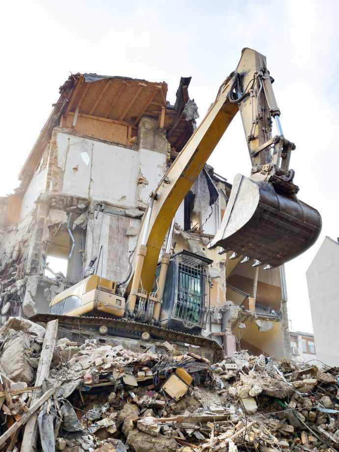 An excavator is demolishing a building with a large bucket.