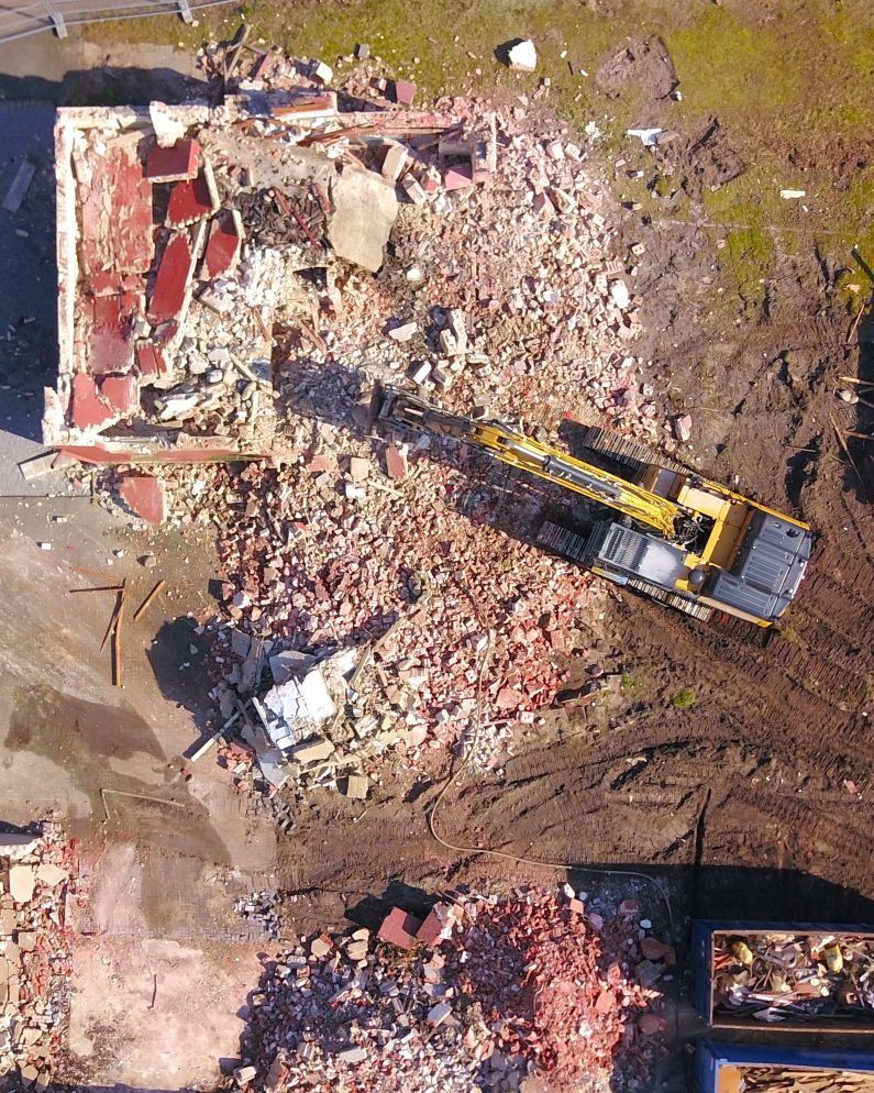 An aerial view of a building being demolished with a yellow excavator.