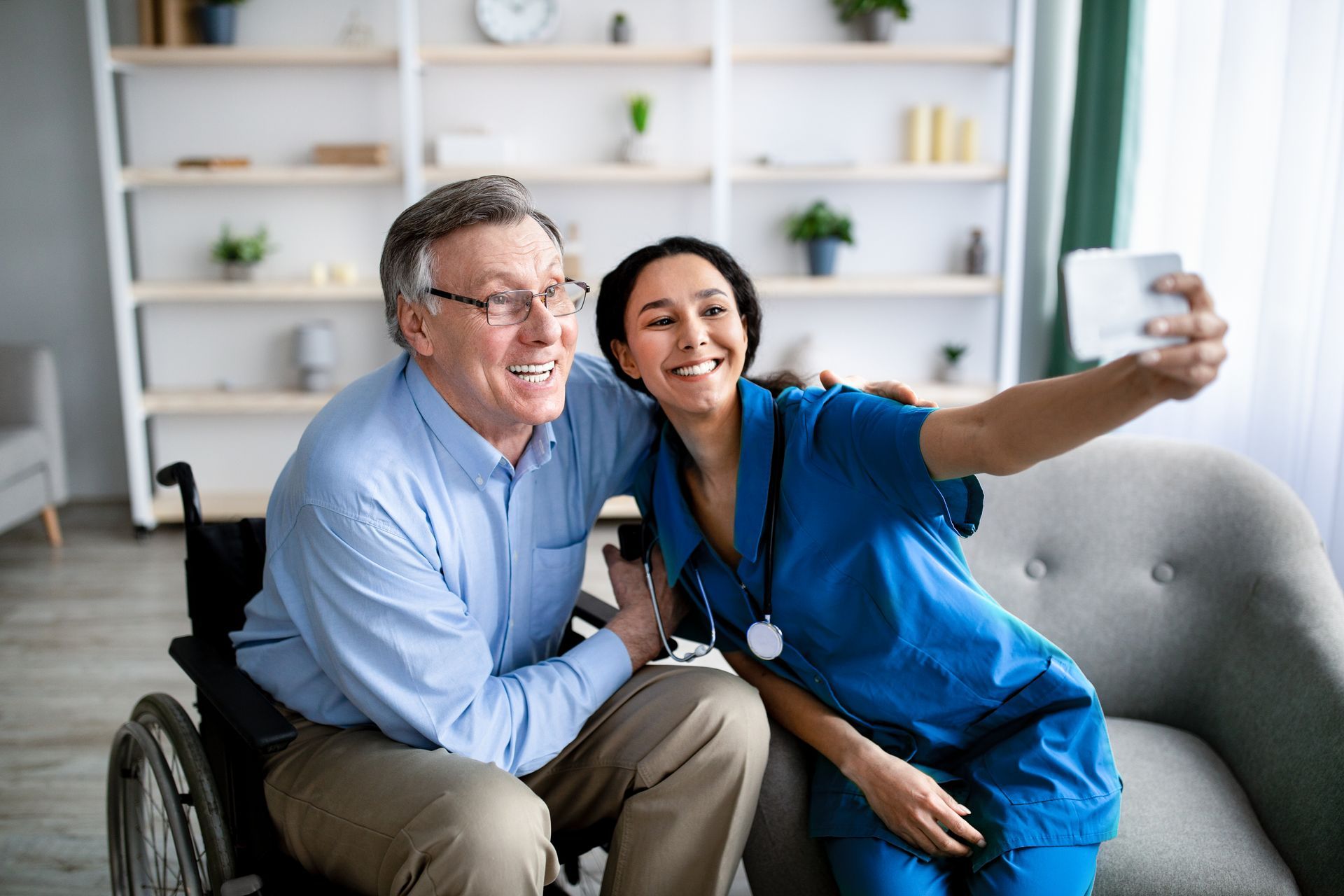 A nurse is taking a selfie with an elderly man in a wheelchair.