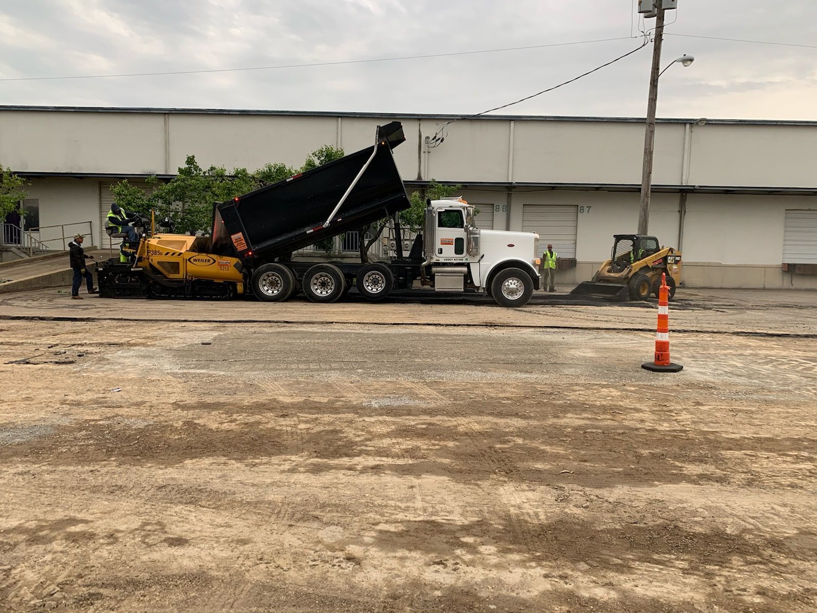 A dump truck is being loaded with asphalt in a parking lot.