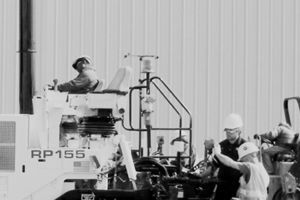 A group of construction workers are working on a machine in a black and white photo.