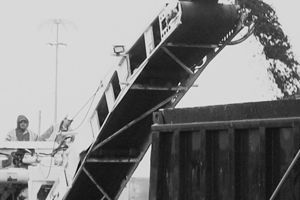 A black and white photo of a conveyor belt pouring dirt into a dumpster.