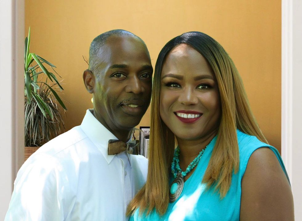 Smiling couple; man in white shirt with wooden bowtie; woman in turquoise top, both in front of tan wall.