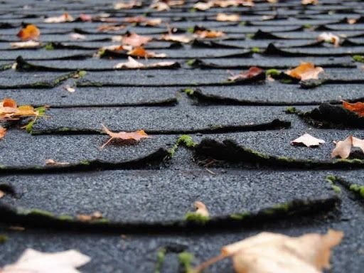 A close up of curled roof shingles with leaves on it.