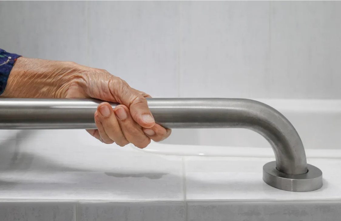 Hand gripping a silver grab bar in a tiled bathroom for support.