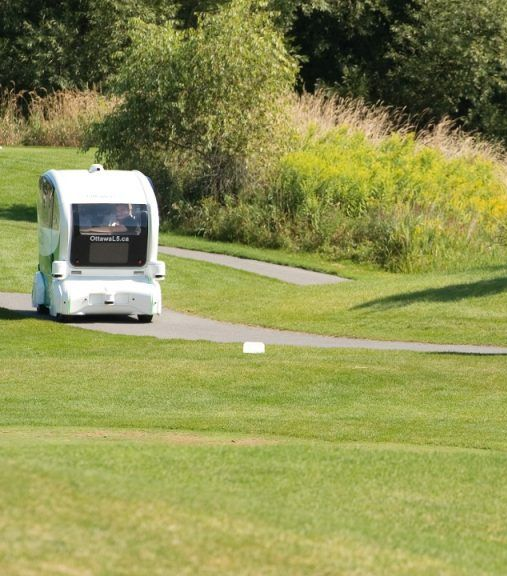Autonomous golf cart driving on a course, white and green.