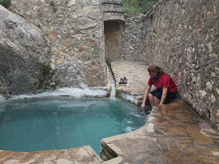 Woman checking water in a stone-walled pool. Clear turquoise water, stone walkway.