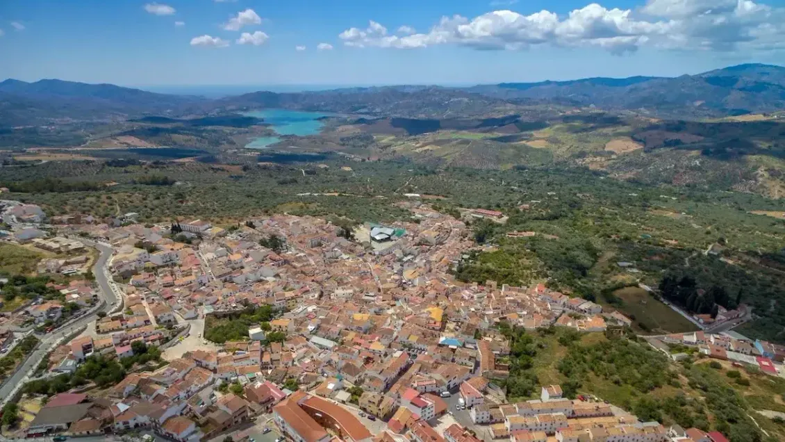 Aerial view of a town nestled in a valley with mountains and a lake in the distance under a blue sky.