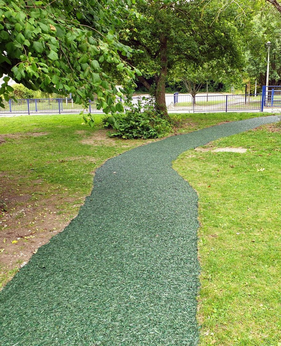 Green rubberized path curves through a grassy park, leading towards trees and a fence.
