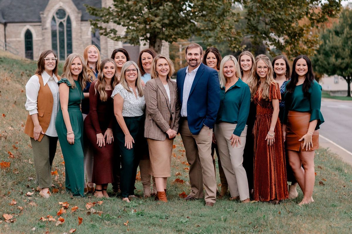 Six women posing on outdoor steps, building background. Variety of outfits, smiles.