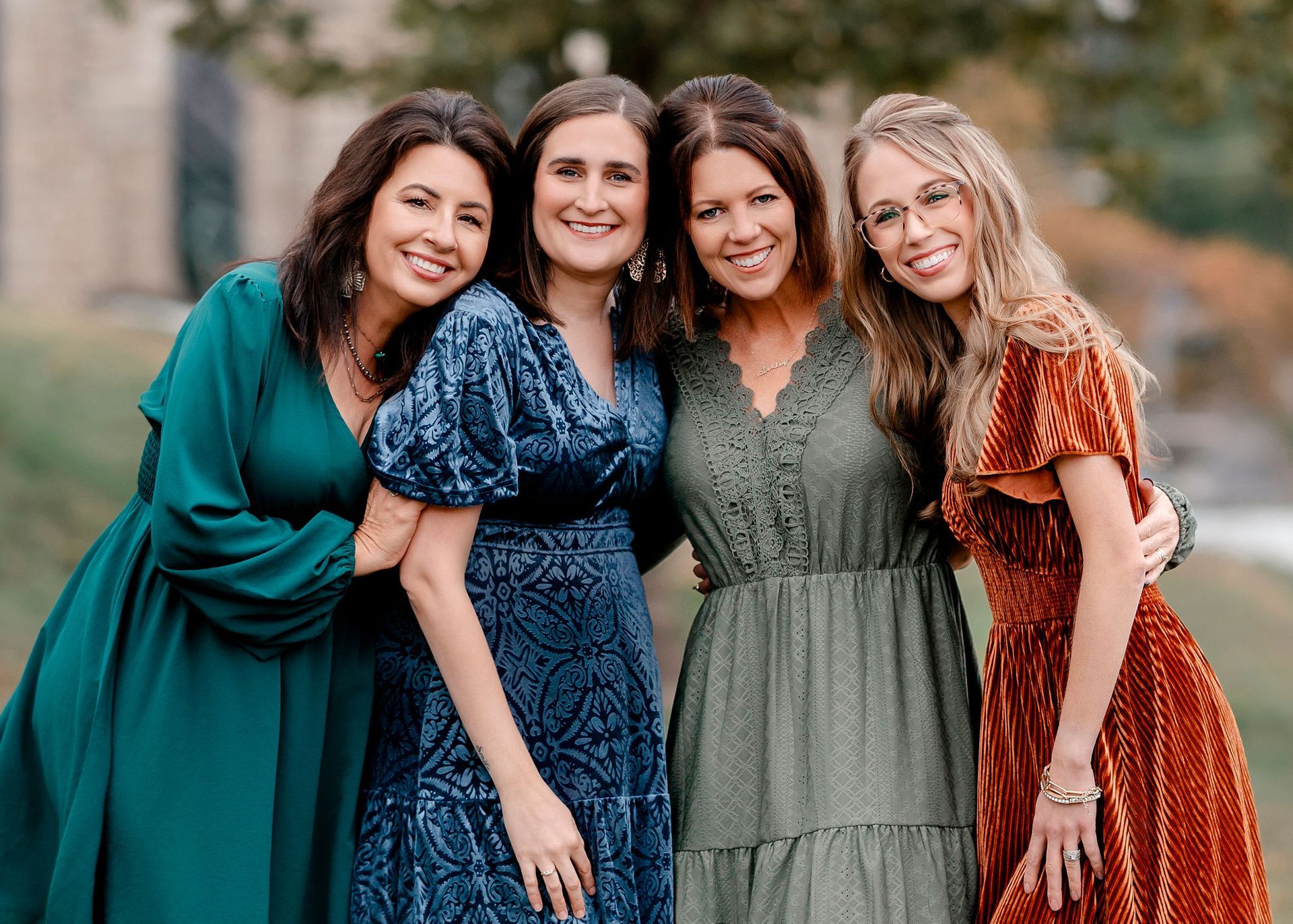 Group of people standing outside a brick building. People smiling, wearing various business casual attire. Sunny day.