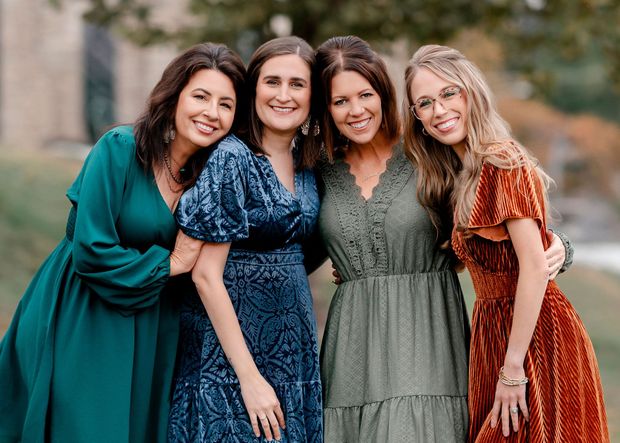 Group of people standing outside a brick building. People smiling, wearing various business casual attire. Sunny day.