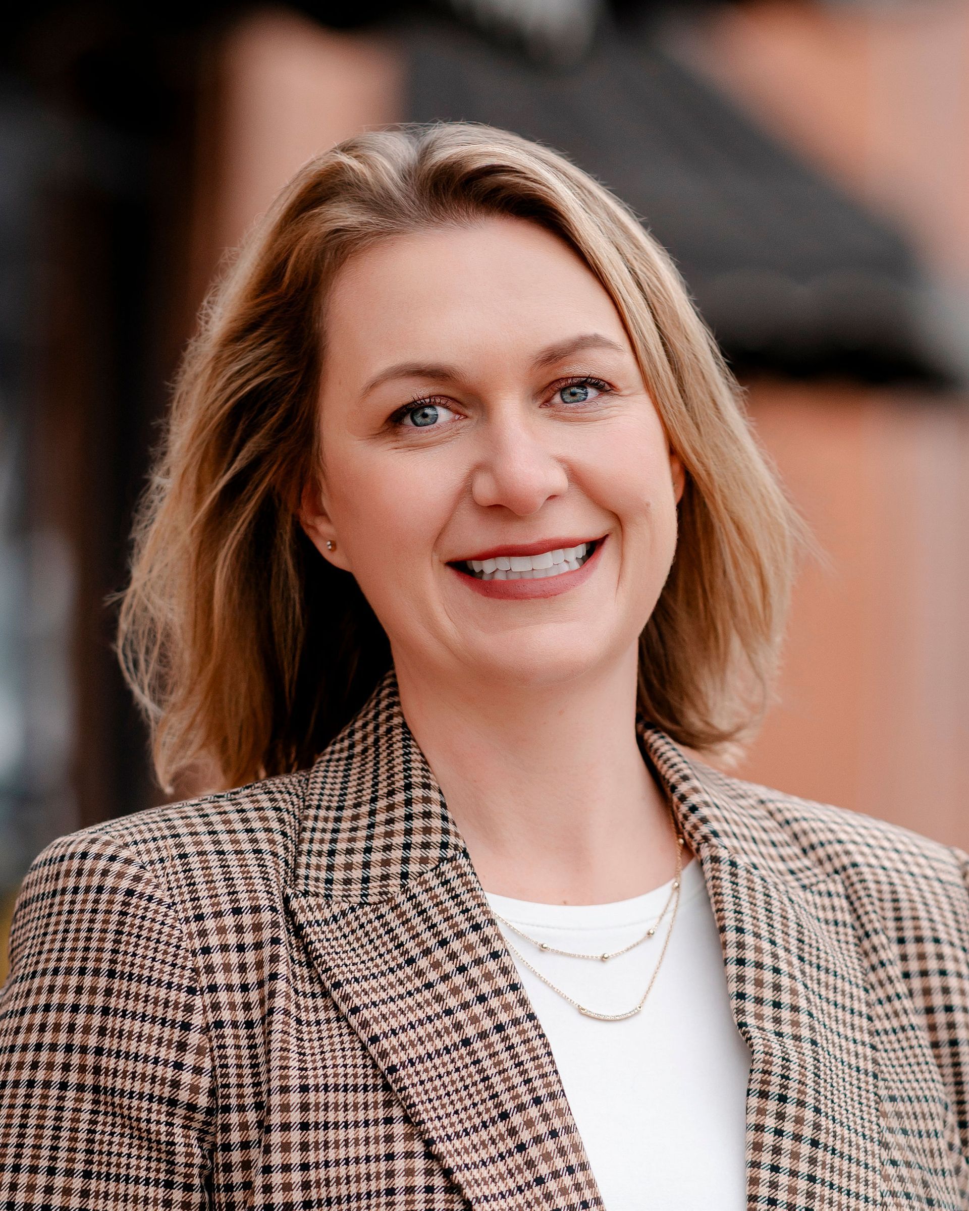 Woman in a tan blazer smiling, close-up portrait.