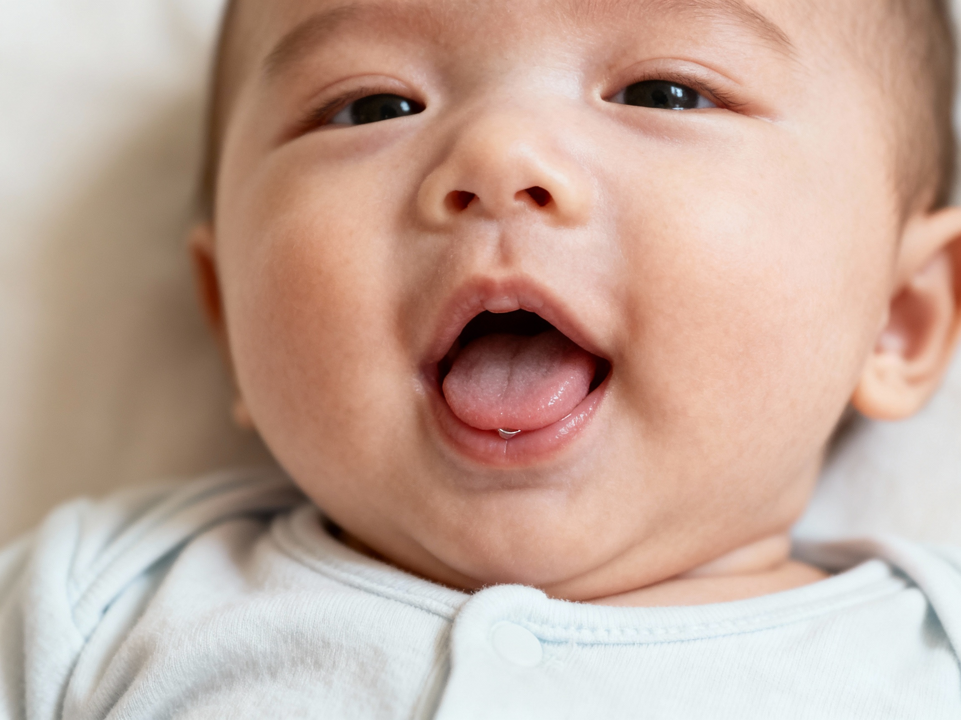 Baby sticking out tongue, holding onto a stroller bar; smiling.